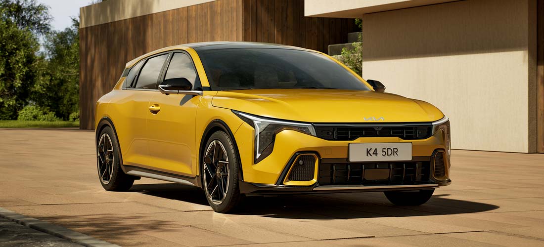 Nowa Kia K4 w żółtym kolorze – elegancki sedan o sportowym charakterze przed nowoczesnym budynkiem